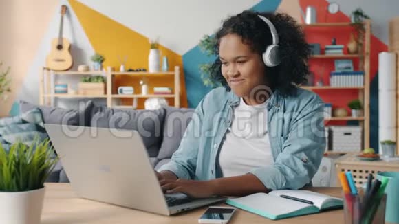 戴耳机的漂亮女士在公寓里听音乐喜欢用手提电脑打字视频的预览图