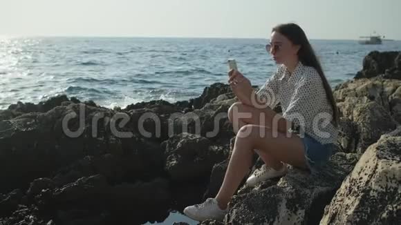 女人正在拍坐在石头上的海景照片视频的预览图