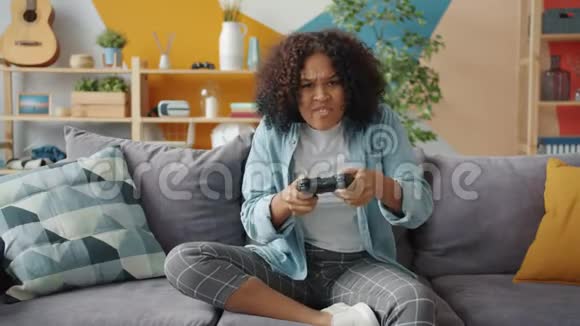 非裔美国女孩坐在沙发上享受电子游戏的肖像视频的预览图