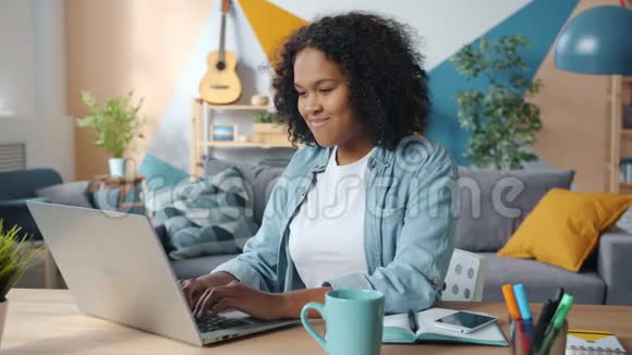 美国黑人女孩在公寓里使用笔记本电脑在室内微笑打字视频的预览图