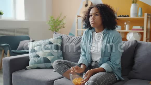 穿着衣服的女孩在电视上观看令人震惊的视频表达了对在家吃零食的恐惧视频的预览图