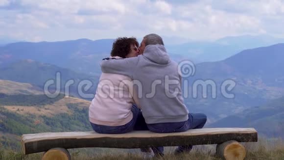 坐在木凳上的老年旅行者拥抱并欣赏山景视频的预览图