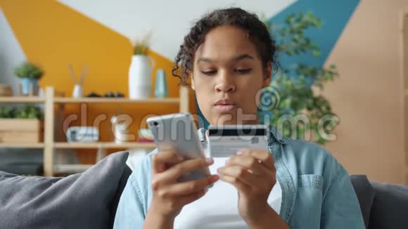 很高兴非洲裔美国女孩微笑着用银行卡和智能手机在线支付视频的预览图