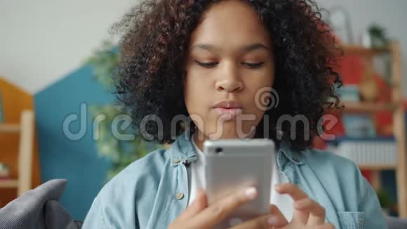 一位漂亮的美国黑人女士在家里用智能手机发短信微笑视频的预览图