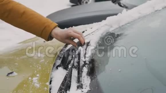 穿着暖棕色夹克的女人在院子里清理挡风玻璃雨刷的积雪视频的预览图
