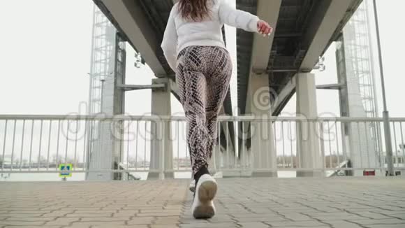 穿着白色夹克和紧身裤的年轻运动女孩跑到栏杆前停了下来这一幕是在高桥的城市公园拍摄的视频的预览图