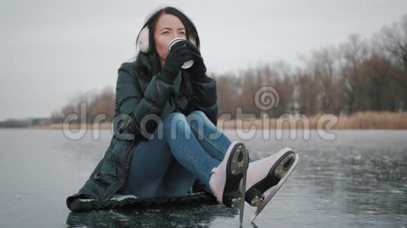 女孩喝咖啡打算滑冰冬天休闲冬天年轻女子在冰冻的湖面上滑冰人民视频的预览图