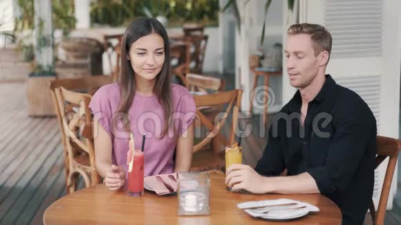 在咖啡馆里的年轻夫妇喝着新鲜果汁谈笑风生视频的预览图