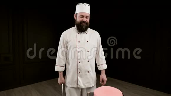 男人在黑色背景下做饭拿着大刀瞄准蛋糕上的一击特写视频的预览图