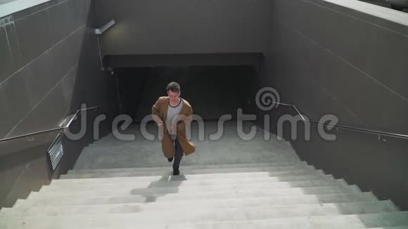 快乐的年轻人在散步时积极跳舞从地下通道上升楼梯他穿一件棕色的长外套视频的预览图