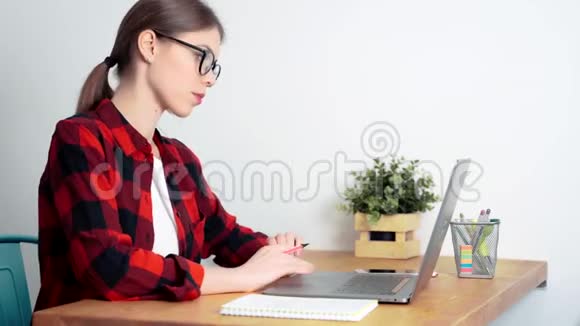 一个年轻的白人女学生在家里用笔记本电脑准备考试或做家庭作业视频的预览图