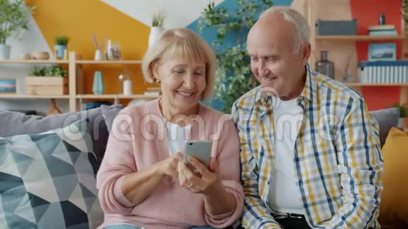老女人用智能手机触摸屏幕与老丈夫在沙发上放松视频的预览图