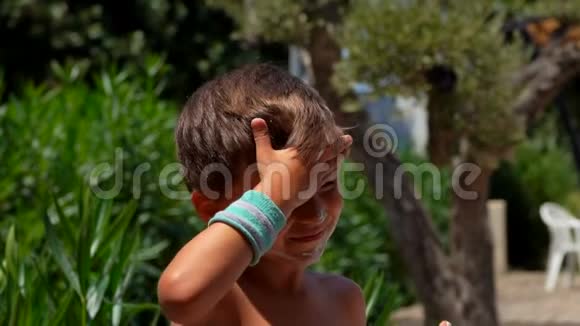 一个晒黑的小男孩在户外用防晒霜涂抹脸颊视频的预览图