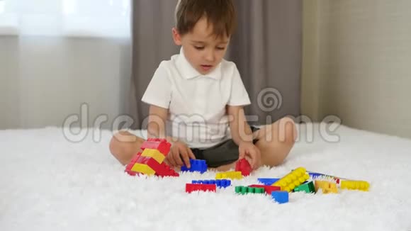 一个快乐的孩子坐在一个房间的床上用彩色的积木搭建玩耍和想象建筑概念视频的预览图
