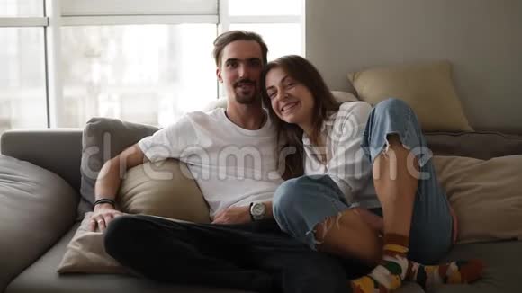年轻白种人的肖像画微笑着胡须男女朋友坐在灰色的沙发上向他摆姿势视频的预览图