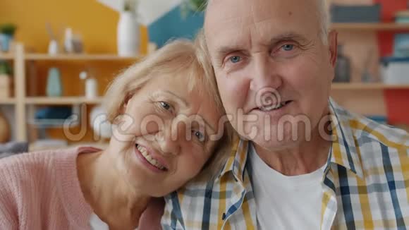 一对恩爱夫妻在家看镜头时微笑的老人和男人的画像视频的预览图