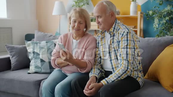快乐的老年夫妇在家中使用智能手机享受社交媒体视频的预览图