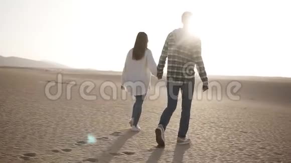 在阳光和蓝天的沙漠下情侣牵着手在浪漫的关系中行走的罕见景象两个年轻的情人视频的预览图