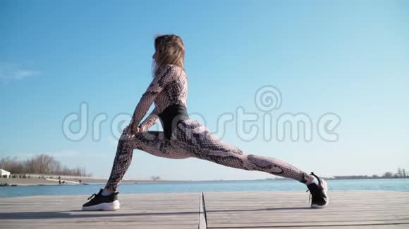 年轻健康的运动型黑发女孩在蓝色湖泊的背景下锻炼户外做运动和健身训练视频的预览图