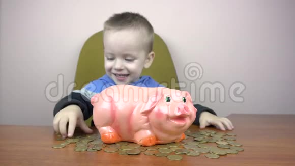 快乐男孩的孩子把硬币扔进小猪储蓄罐省钱的概念视频的预览图