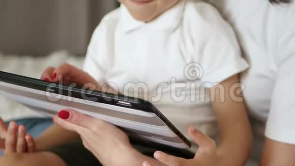 一个小孩坐在母亲的膝上专注地看着平板电脑屏幕妈妈拥抱她的儿子快乐的概念视频的预览图