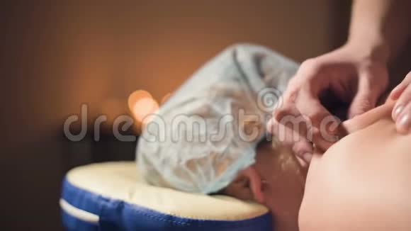 年轻的男性按摩治疗师在按摩室里对有纹身的女人做肩部按摩按摩室里光线昏暗视频的预览图