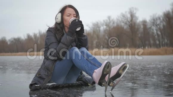 女孩喝咖啡打算滑冰冬天休闲冬天年轻女子在冰冻的湖面上滑冰人民视频的预览图