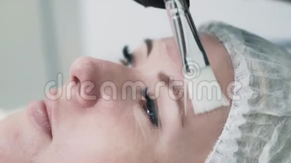 戴手套的美容师在治疗前在妇女脸上涂上特殊的凝胶视频的预览图