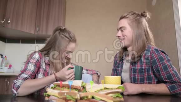 年轻夫妇坐在厨房里从杯子里喝酒聊天特写视频的预览图