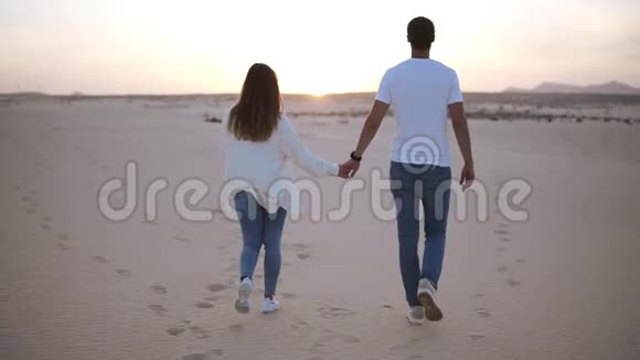背面的镜头牵手情侣在阳光和蓝天的沙漠下浪漫地走着两个年轻人视频的预览图