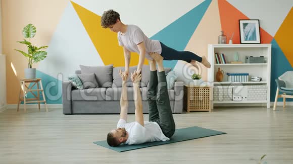 快乐的一对在家做双人瑜伽男人抱着女人腿在地板上视频的预览图