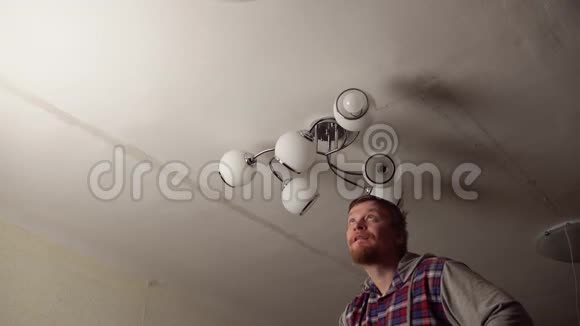 男电工正在把灯泡拧成天花板下的玻璃吊灯视频的预览图