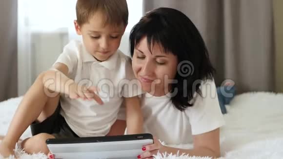 一对母子躺在沙发上用平板电脑上的儿童应用程序看游戏幸福的概念视频的预览图