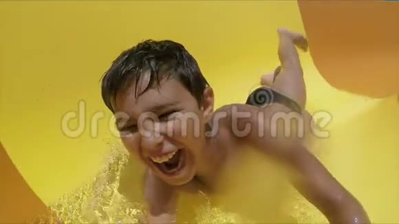 笑的男孩在一个水上公园里趴着沿着橙色的滑梯视频的预览图