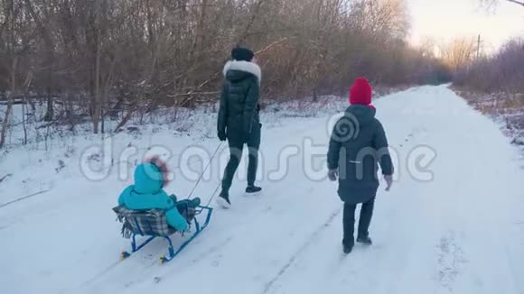 十几岁的女儿和母亲拉着小儿子在雪橇上跑剪影一家人在冬天玩积极健康视频的预览图