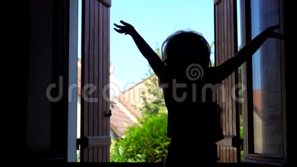 一个快乐的小女孩在开着的窗户旁边的床上跳跃的剪影视频的预览图