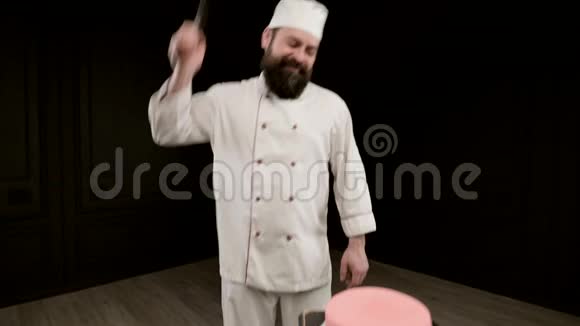男人在黑色背景下做饭拿着大刀瞄准蛋糕上的一击特写视频的预览图