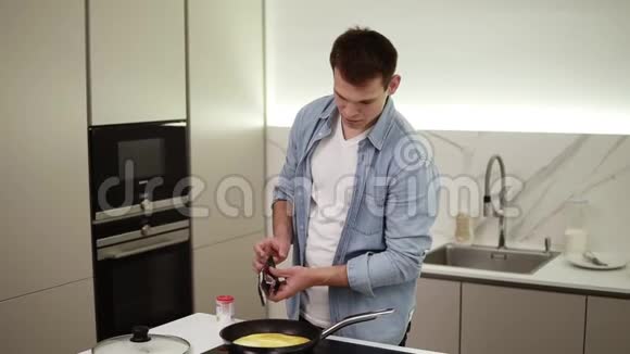 厨房里的人帅哥在做早餐做煎蛋加入香料盐胡椒快乐的男人视频的预览图