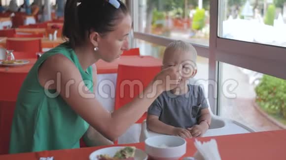 一位年轻的母亲早上在一家咖啡馆里在一张桌子上喂她可爱的小儿子视频的预览图