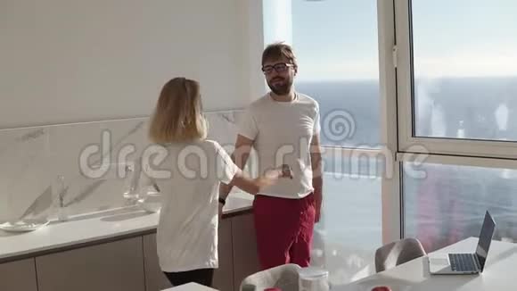 年轻夫妇早上在厨房和全景窗会面妻子在丈夫的拥抱跳跃视频的预览图