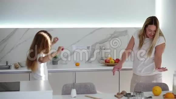 幸福的家庭在现代白色的厨房妈妈和女儿穿着白色便服放松地跳舞妈妈在跳舞视频的预览图