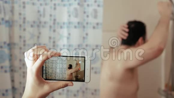 快乐有趣的人洗澡跳舞唱歌女性手握电话拍摄丈夫的照片视频的预览图