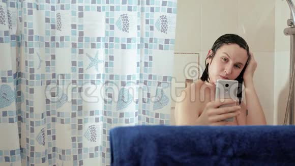 淋浴女孩在智能手机中使用互联网阅读新闻社交网络她的头上涌着水慢动作视频的预览图