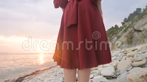 太阳落山时一个赤脚女孩穿着一件红色的裙子在风中飘动她的腿后面做了一个动作视频的预览图
