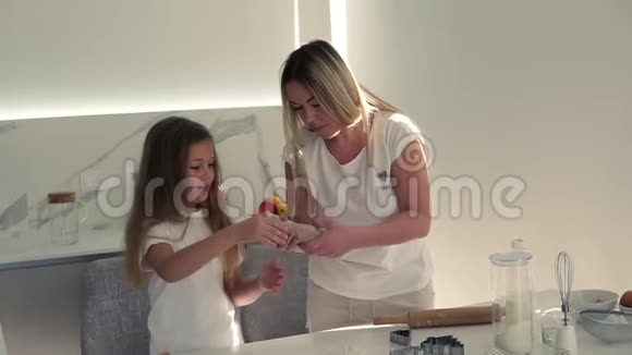 可爱的妈妈教可爱的女儿揉面团有趣的女孩帮助妈妈准备饼干在里面玩视频的预览图