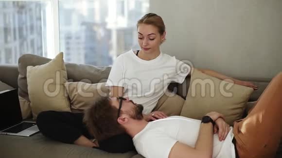 一对夫妇在沙发上放松享受他们的关系并交谈金发女人和男人躺在她身上视频的预览图
