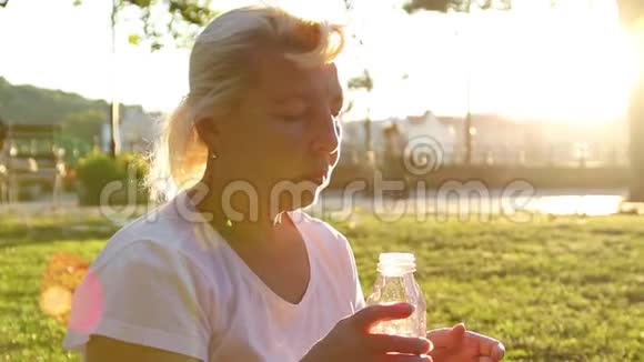 户外娱乐活动成年妇女坐在公园里在阳光下从塑料瓶里喝水视频的预览图