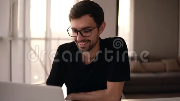 戴着笔记本电脑戴着眼镜的牙齿微笑男人的肖像自由职业者在家工作电脑勇敢的男人视频的预览图