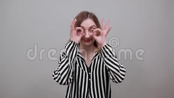 白种人女人看着摄像机用手指在眼睛上做眼镜手势视频的预览图