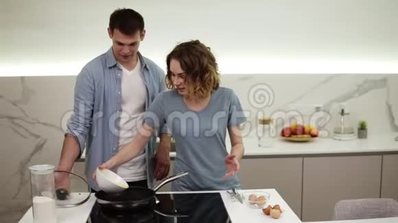 快乐的情侣一起做早餐女孩把混合鸡蛋从碗里倒进厨房炉子上的火锅里丈夫视频的预览图